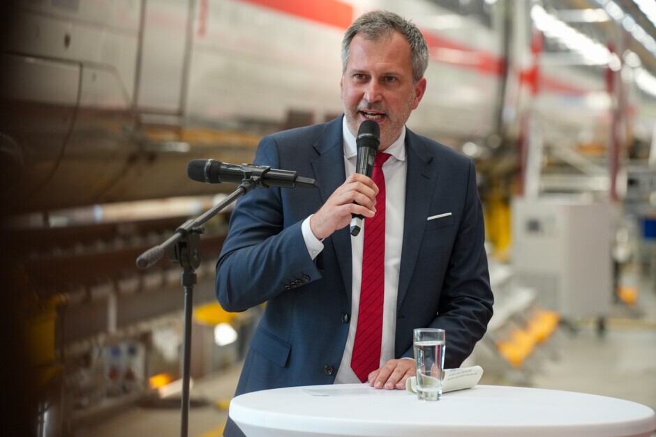 Cottbus/Chóśebuz, 6. Juni 2025 – Stolze 22 Jahre war ein ICE 2 der Deutschen Bahn (DB) mit Wappen und Namen der Stadt Cottbus auf Deutschlands Schienen unterwegs. Jetzt übernimmt ein hochmoderner zwölfteiliger ICE 4 der DB die Aufgabe des rollenden Botschafters für die Stadt am Rande des Spreewalds. Regionaltypisch mit Spreewälder Gurkenwasser wurde der ICE-Triebzug 9009 (ICE 4 Baureihe 412) im neuen Werk der DB in Cottbus/Chóśebuz getauft. Brandenburgs Ministerpräsident Dr. Dietmar Woidke, der Cottbuser Oberbürgermeister Tobias Schick, Dr. Daniela Gerd tom Markotten, DB-Vorständin für Digitalisierung und Technik, und Angelina Tantow, Fahrzeuglackiererin in Ausbildung im neuen Werk Cottbus, enthüllten gemeinsam das Stadtwappen und Schriftzug „Cottbus / Chóśebuz“.